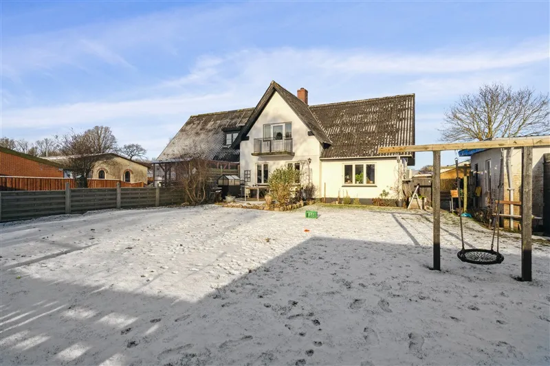 Snehvide fortov med legeplads og huse, træklatring og svingestol i sneen, fredeligt landsted med altan og tagrør