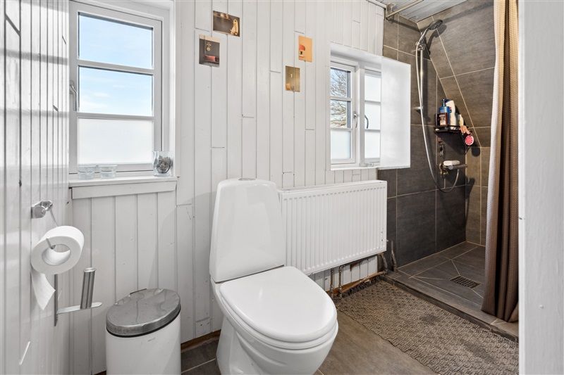 Toiletrum med hvid toilet, radiator, skam, to toiletpapirruller og en lukket garderobe.