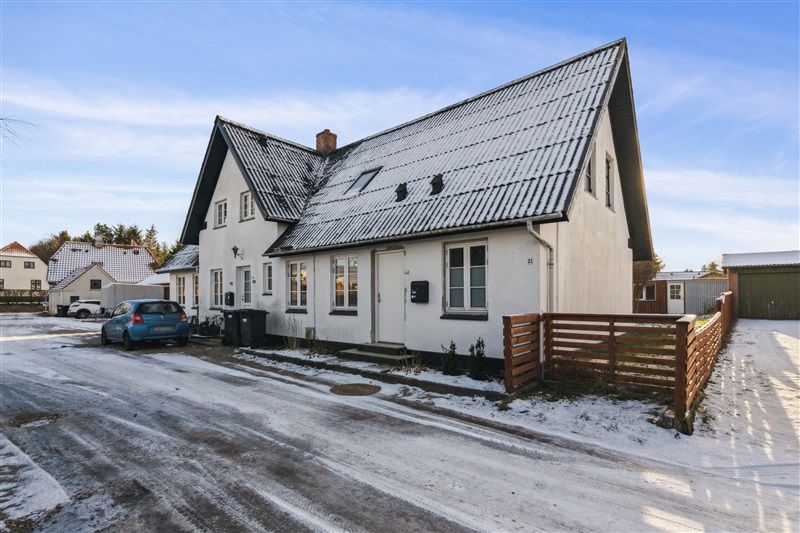 Hvidt hus med garage og skur, snedækket vej, parkerede biler og træhegn