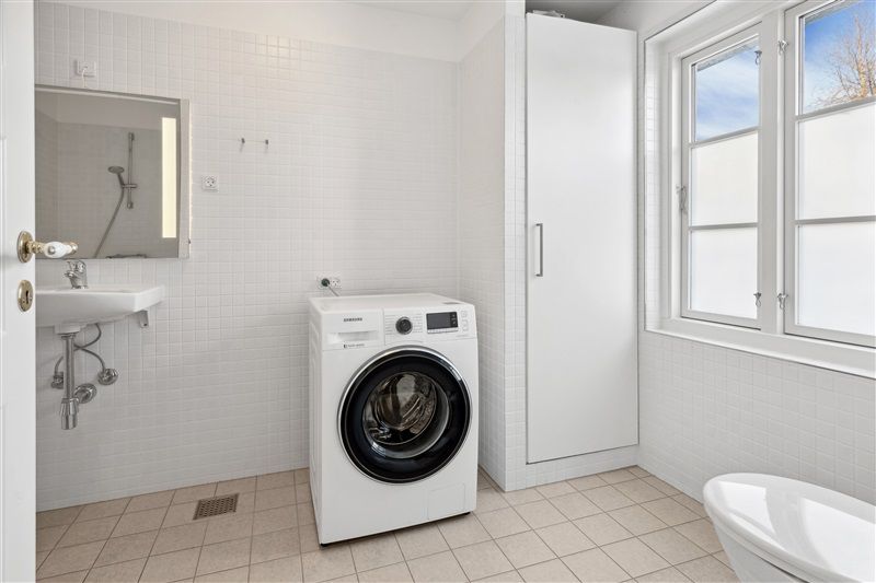 Moderne badeværelse med hvid vasketøjsmaskine, hvidt badekar, hvidt spejl, hvidt håndvask og hvidt badeværelseskab