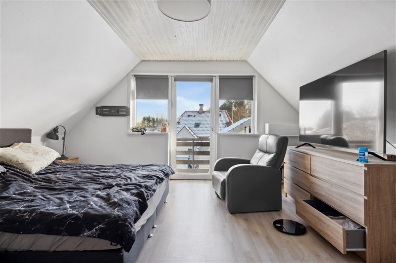 Et soveværelse med loft, højt gulv og moderne møbler, inklusiv seng, lænestol og tv