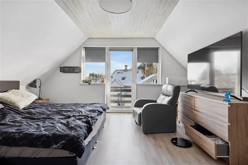 Et soveværelse med loft, højt gulv og moderne møbler, inklusiv seng, lænestol og tv