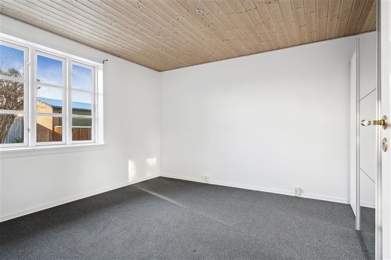 En tom stue med hvide vægge, højt gulv og et vindue med udsigt til en have.