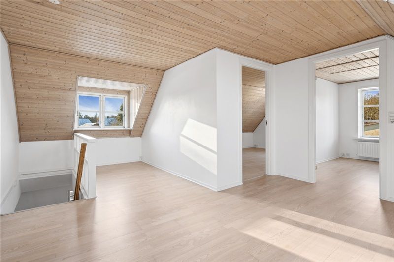 Et lyst værelse med lysegul gulv og hvide vægge samt store vinduer med udsigt til det ydre