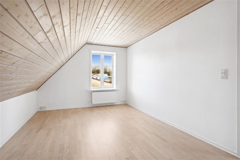 En hvidvægget stue med trægulv og træloft samt et trævindue og radiator i hvidt