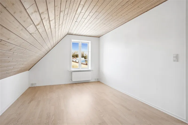 En hvidvægget stue med trægulv og træloft samt et trævindue og radiator i hvidt