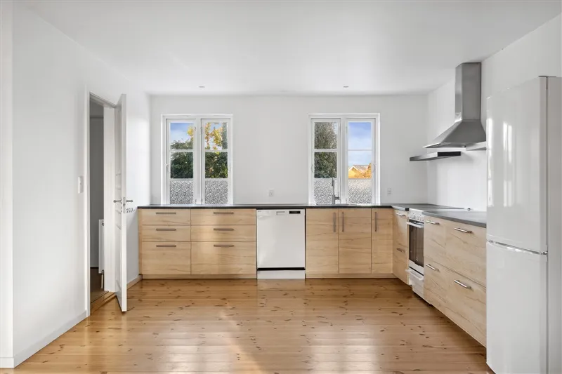 Moderne køkken med lysegul træpanelering og hvide vægge, store vinduer og integreret hvidevarer og apparater