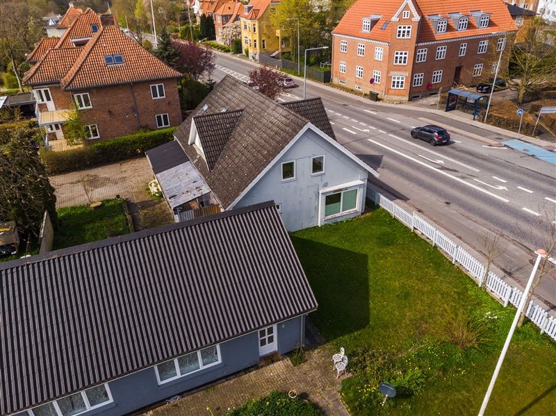 Vej med bil og busstoppested samt huse med forskellige farver og størrelser