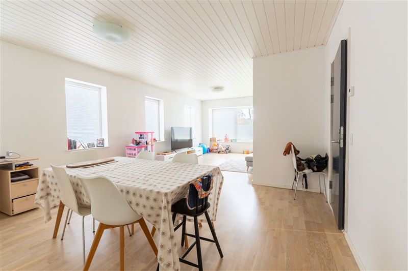 Foto af et rum med lyse vægge og et hvidt loft med hvide loftsbjælker. I midten er der et spiseplads med et rundt bord og