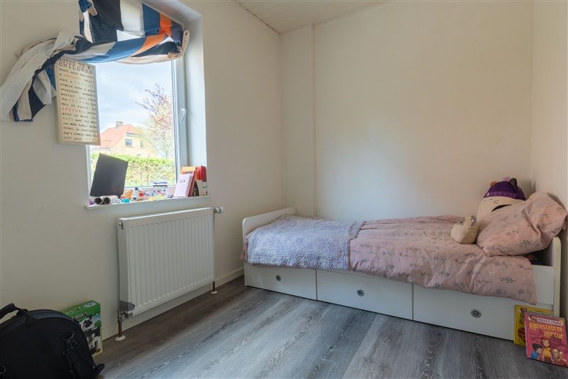 Billede af et barneværelse med hvidt tøj og møbler og en radiator og et vindue med et notat og en bog og et krus i