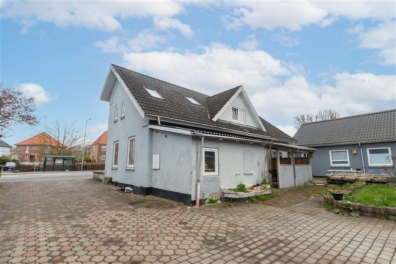 To huse med skifer tag, en stor have og terrasse, parkeringsplads og udsigt til skov og bygninger