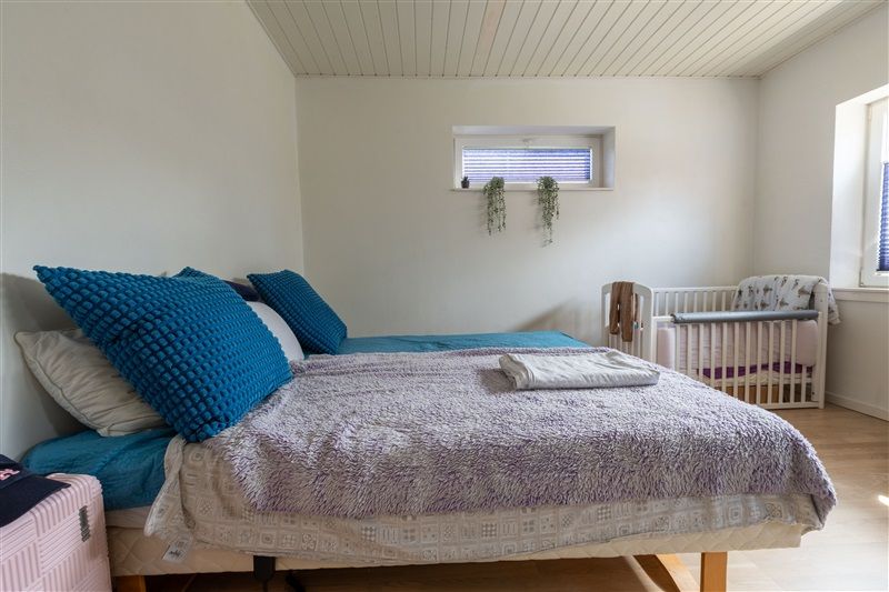 Soveværelse med to senge og en krybbe samt en hængende plante og et vindue med jalousier