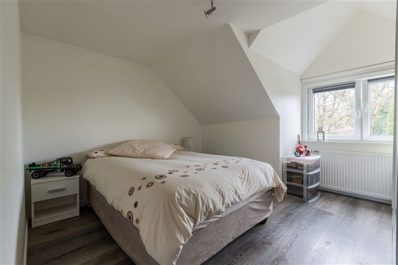 Soveværelse med højloft, hvidt loft, bleggul gulv og et dobbeltseng med hvid dyne og tæpper samt to sideborde og et vindue