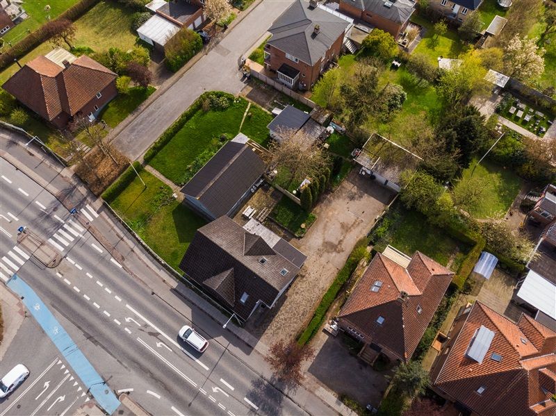 Vejle by med grønne haver, røde tag, hvide og brune huse og veje med biler og cykelstier