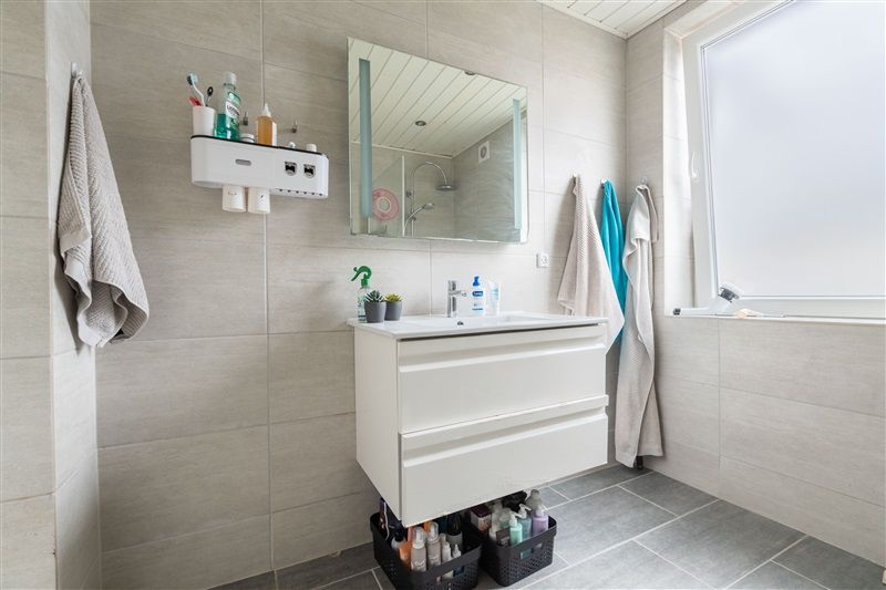 Moderne badeværelse med hvidt vasketøjsskab, spejl og turkis badeværelseshåndklæde hængende på væggen.