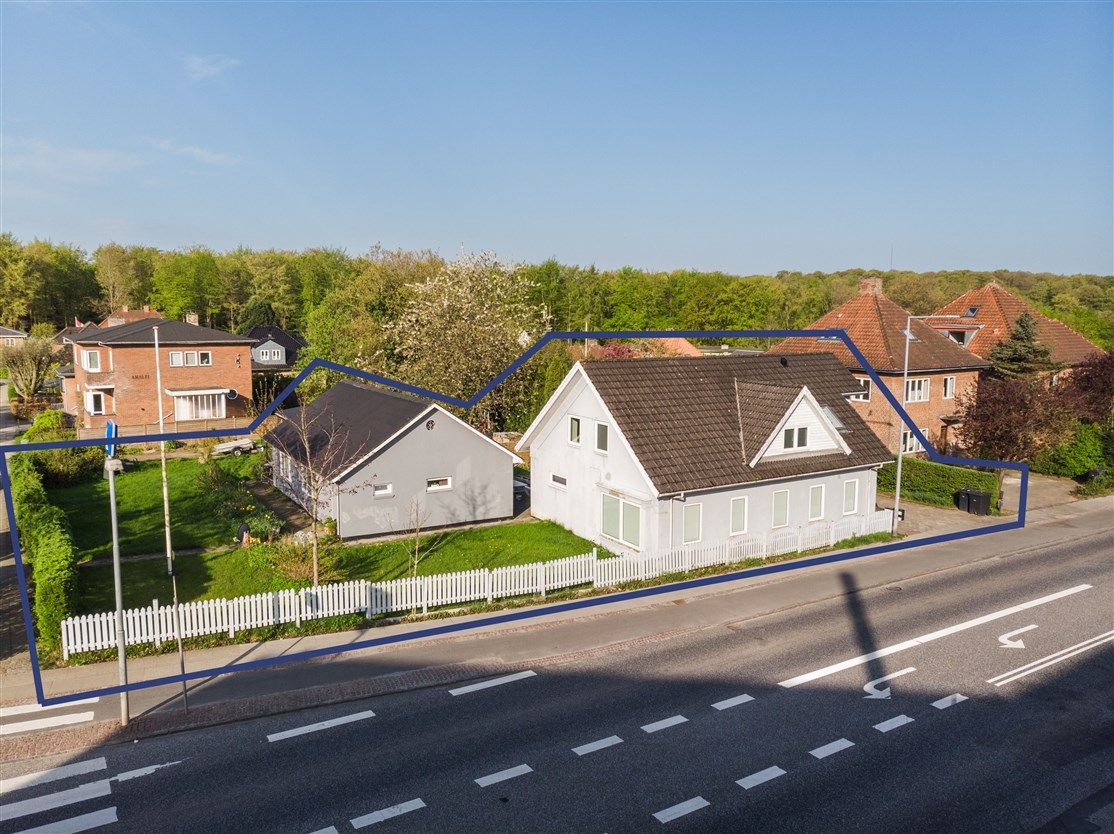 To huse på en gade med tomt og grønne træer i baggrunden, der er markeret med blå linjer