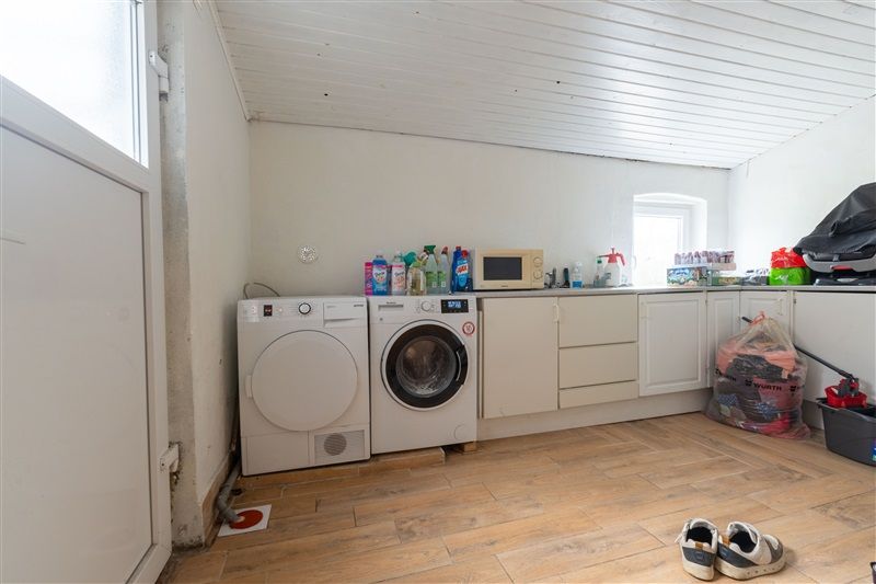 Rum med tøjvask og tøj i poser samt tøjstativ og tøjvask i hvidt og brungul gulv