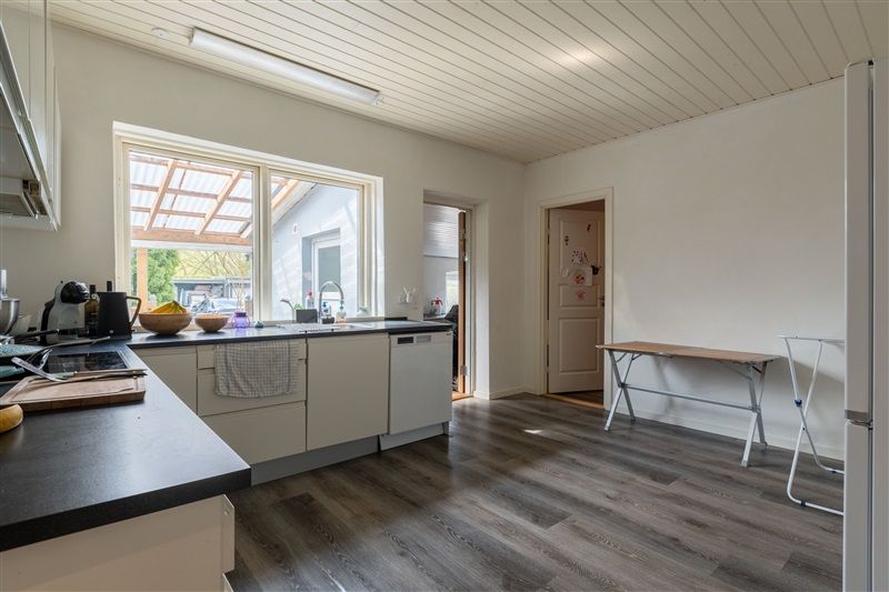 Moderne køkken med hvide vægge, trægulv, hætte over komfuret og et rektangulært bord med høj kant i hjørnet