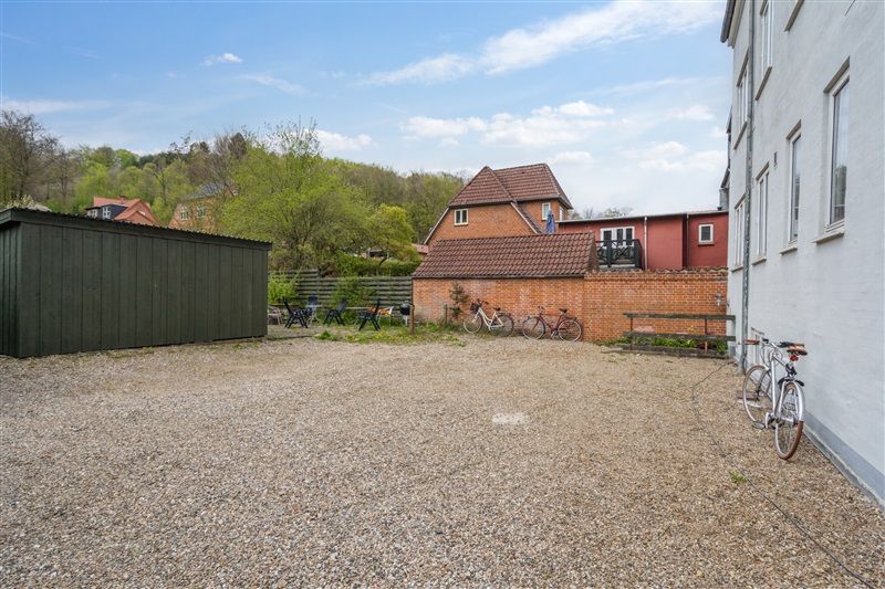 Lejlighedspark med lejemål, hvor der er tre cykler parkeret ved bygningen og flere sæsonmøbler udenfor