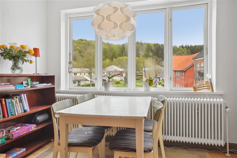 Inde i et velholdt køkken med en hvid spisebord og stole, blomster i en vase og en lysekron over bordet