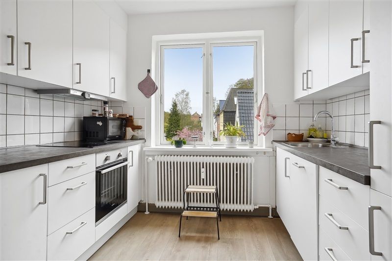 Velholdt køkken med moderne møbler, hvide vægge, køkkenhøj og vinduesvisning med udsigt til træer og bygninger i baggrunden