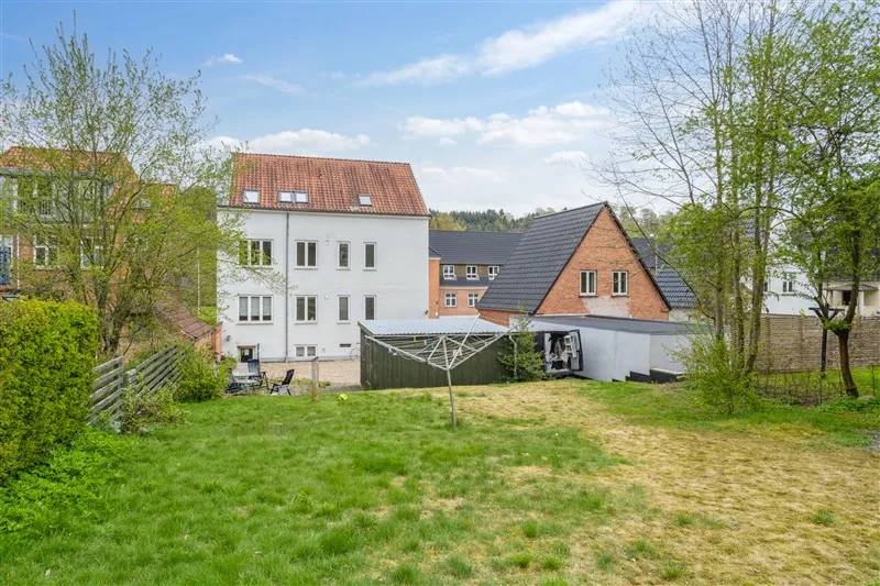 En byggegrund med grønne træer og buske samt lejlighedsbygning med fire lejligheder i Vejle