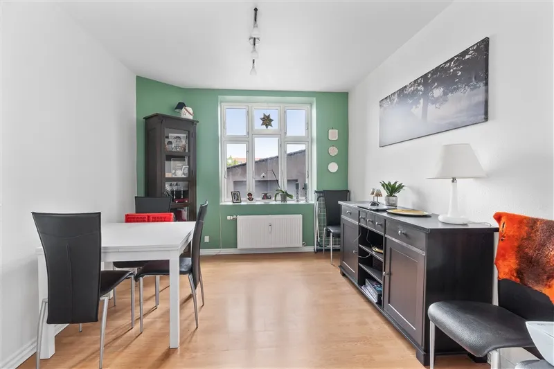 Indenfor er der en spisebord med fire stole og en sofa med orange tæppe samt et bord med lamp og plante