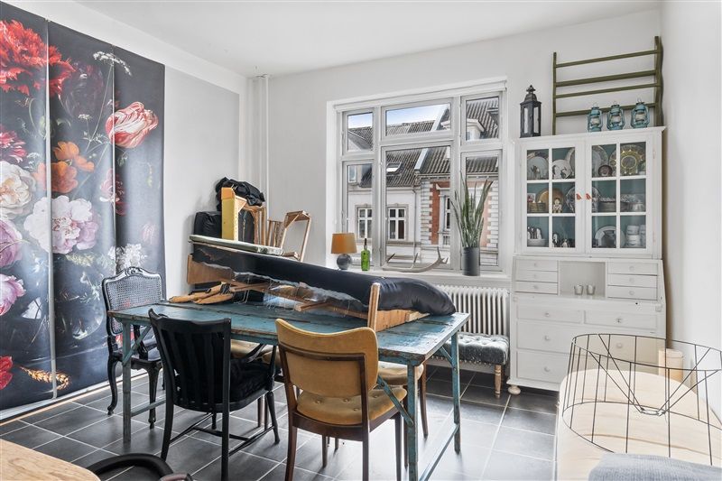 Sort og hvid blomstertapet med røde og gule blomster. Bord med fire stole. Køkken med lyse og hvide møbler. Køkken med lyse