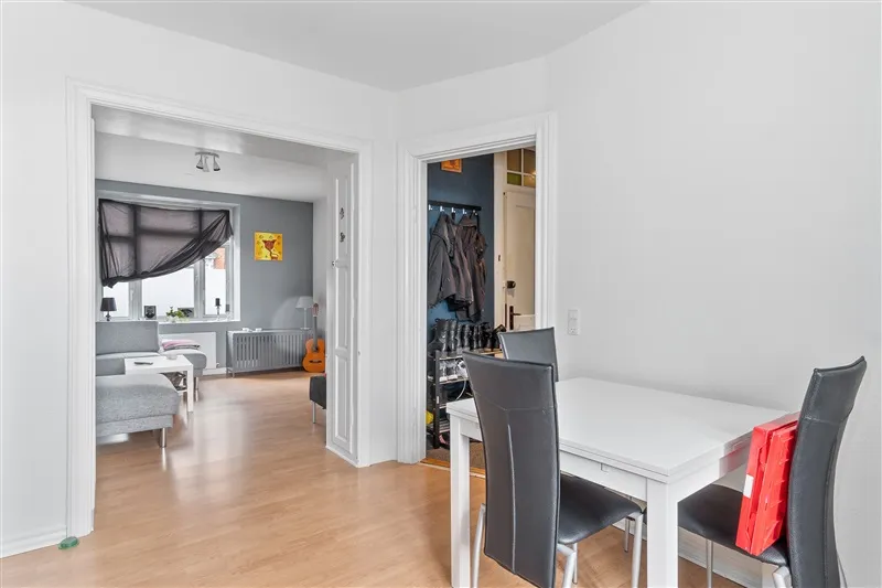 Modernt, minimalistisk stue med hvidt gulv og hvide vægge. Et højt, enkelt bord med fire stole og et rødt opbevaringsskab.