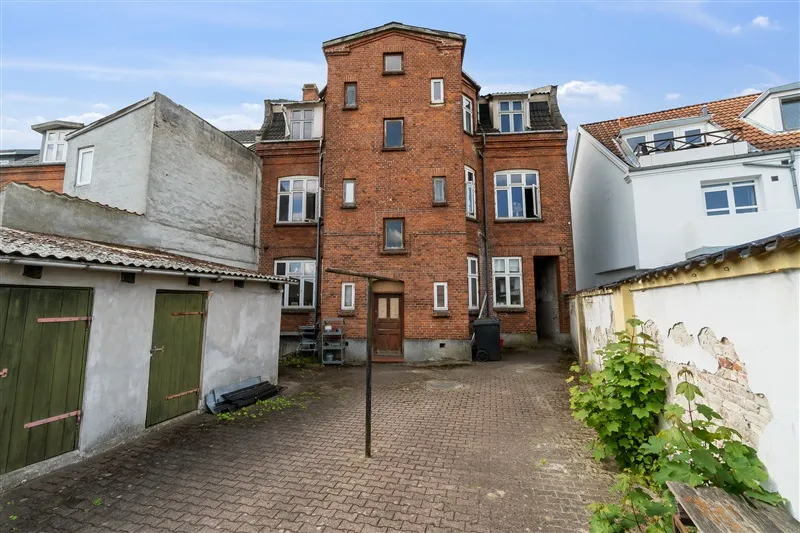 Gamle bygning med rød mursten og flere vinduer og døre i en lille gade i Vejle