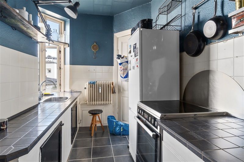 En køkken med blå vægge og hvide kakel, hvide skabe og sort granit beløb, en hvid køleskab og en ovn, og et bord med en