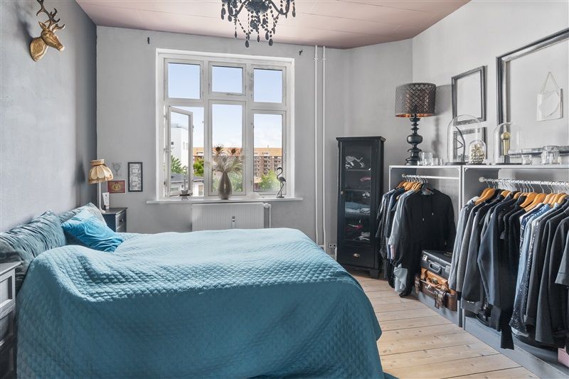 En soveværelse med tæppe, to senge med blå hovedpuder, tæppe og tæppe på gulvet, trægulv og udsigt til bygninger fra vinduet