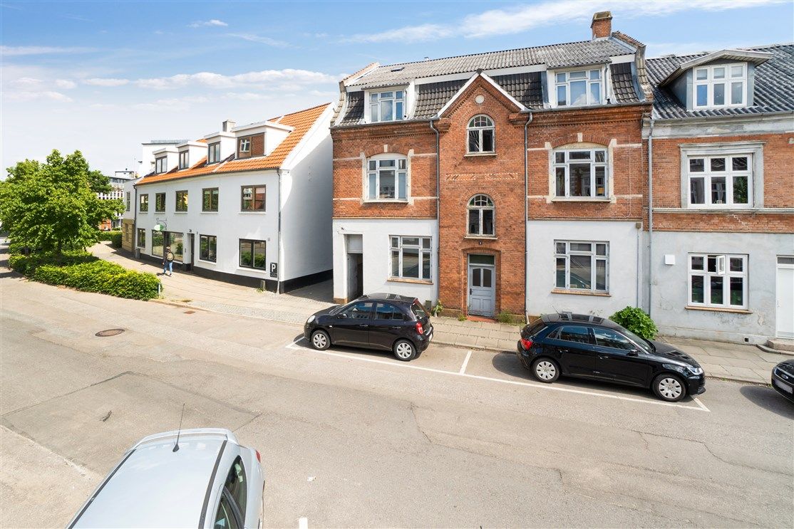 Tre biler parkeret på en sidevej med rækkehuse i baggrunden og en person der går