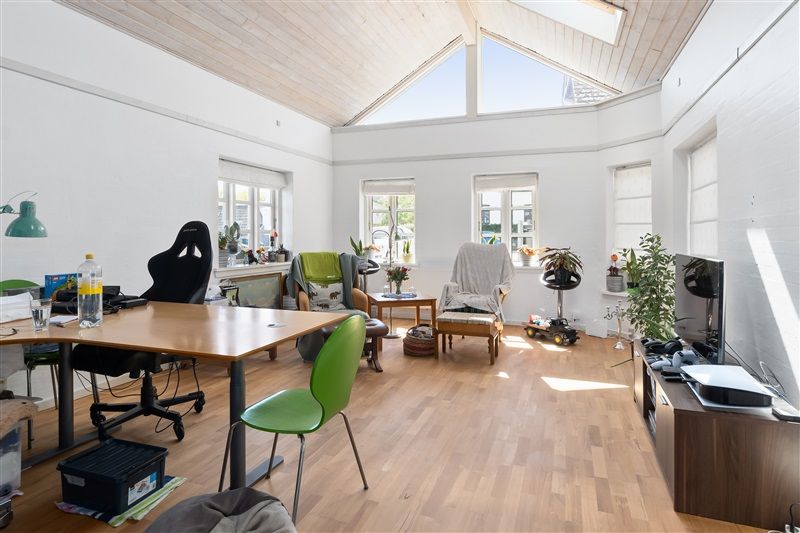 Kontor med højt loft, lysevinduer, gulv, borde, stol, sofa, TV, lampe, plante og vase med blomster