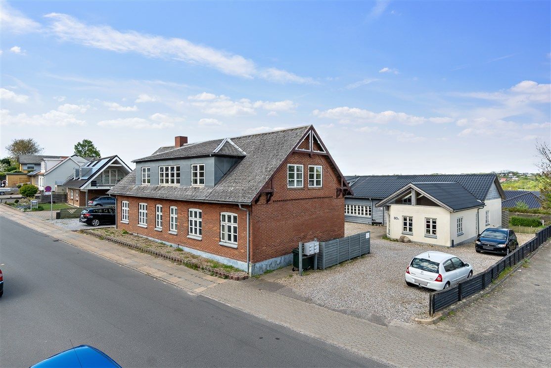 En række huse med garager og parkerede biler i en landsby med små bakker og træer i baggrunden