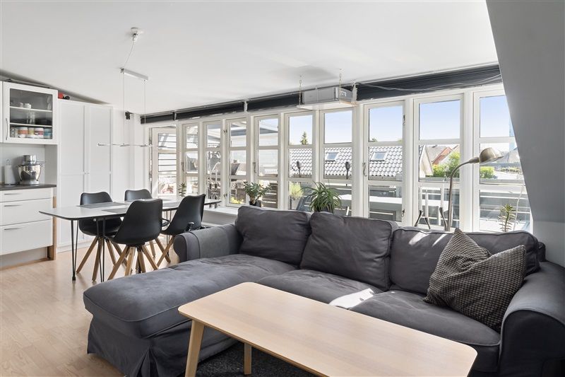 Lejlighed med lyse, moderne indretning, lysegrå sofa, lyse træbord og sort spisestuebord med stolpe og træstole