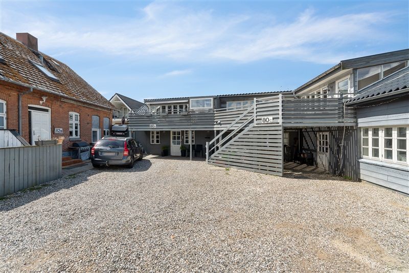 Lejlighedsbyggeri i Kolding med terrasse og parkeringsplads, nummer 80 og 82, lejlighedsindgang, træskur og bilparkering