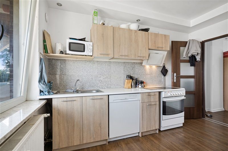 Rent og funktionelt køkken med moderne hvide kakel og lyse træskabe. Komplet med komfur, vaskemaskine og mikrobølgeovn.