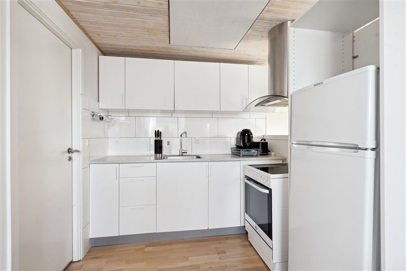 En moderne køkken med hvide vægge, hvide skabsfronter og en hvid ovn og køleskab samt en sink med vandhane