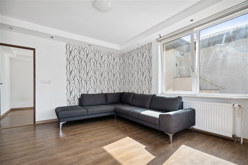 En moderne stue med lyse trægulve og hvide vægge samt en stor sektionssofa og et hvidt radiatorpanel