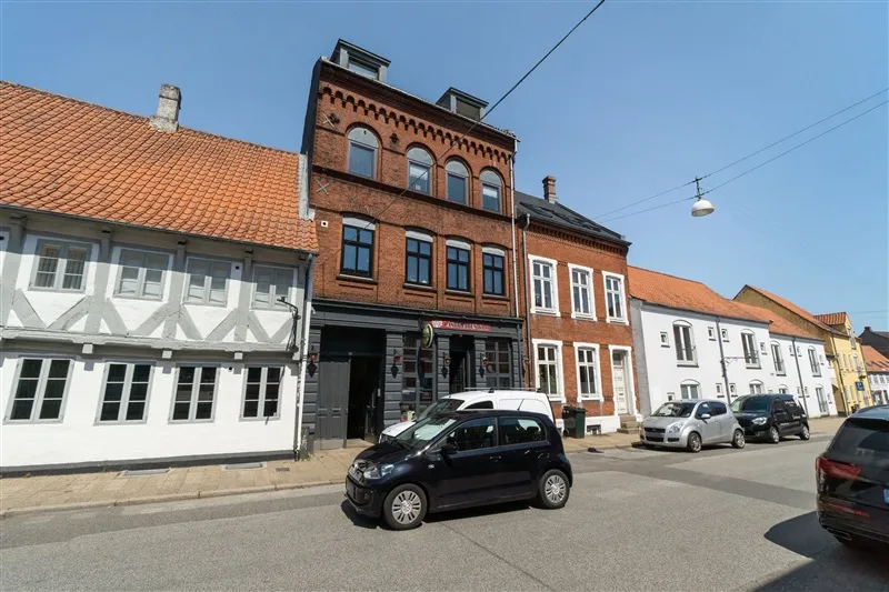 Udlejningsejendom i Kolding med flere biler parkeret foran og røde tag.
