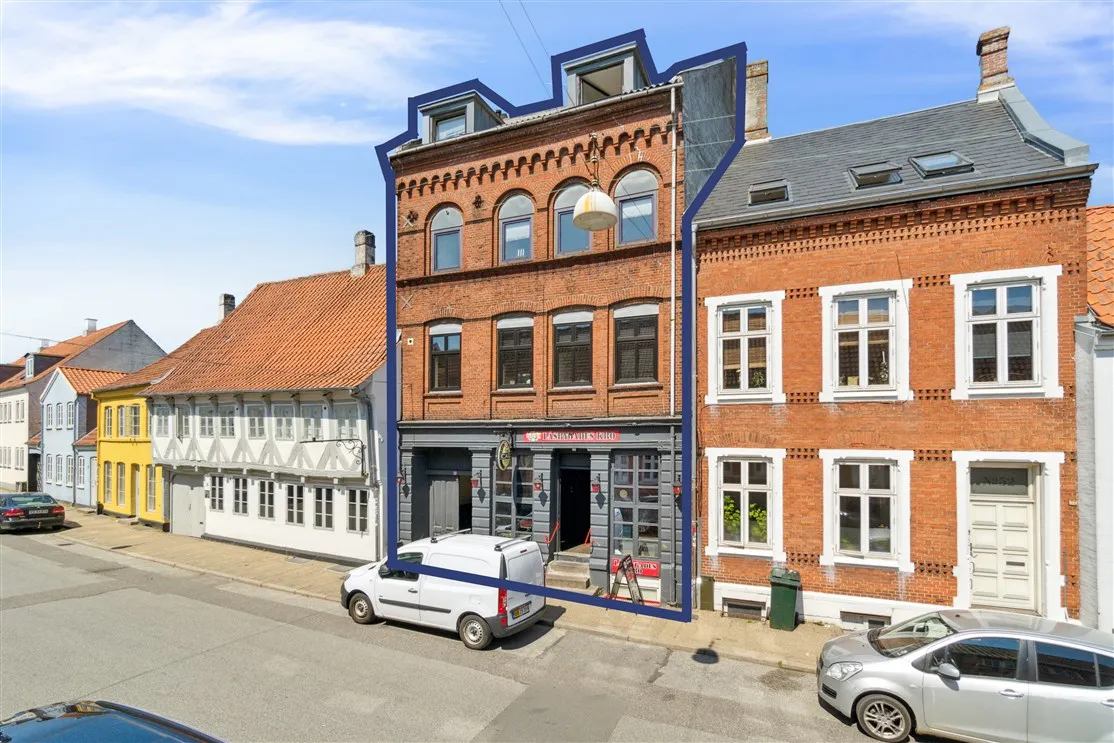 Et stort rød murstenshus med store vinduer og to biler parkeret udenfor