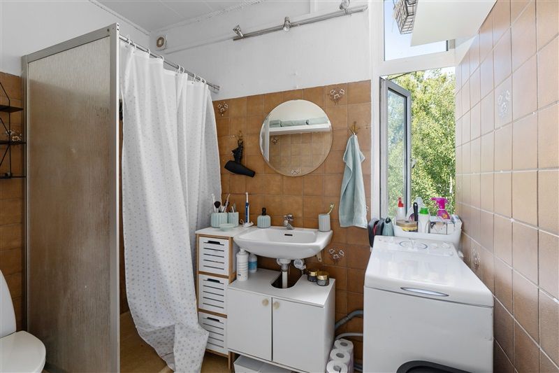 En lille badeværelse med hvidt badekar, vask og håndklædeholder samt en moderne hvid toilet.