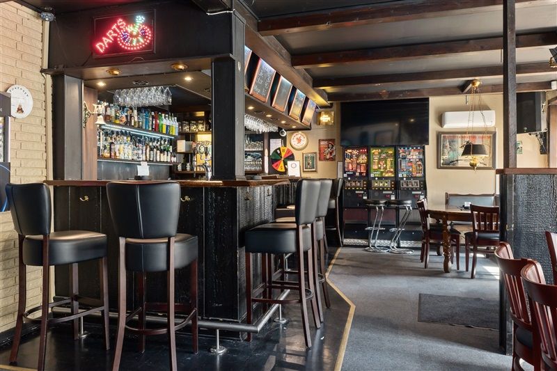 Barstol i sort læder, bardisk og flere spilautomater i en hyggelig bar.