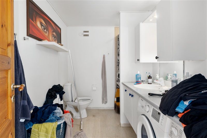 En vaskemaskine og toilet i et badeværelse med et loftsskab, hvor der er en tørretumbler og et hængeloft.