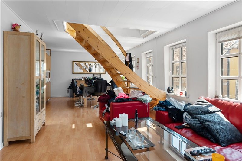 Et lyse og pænt værelse med højloft og trætrapper, to røde sofaer og spisestuebord med to stearinlys