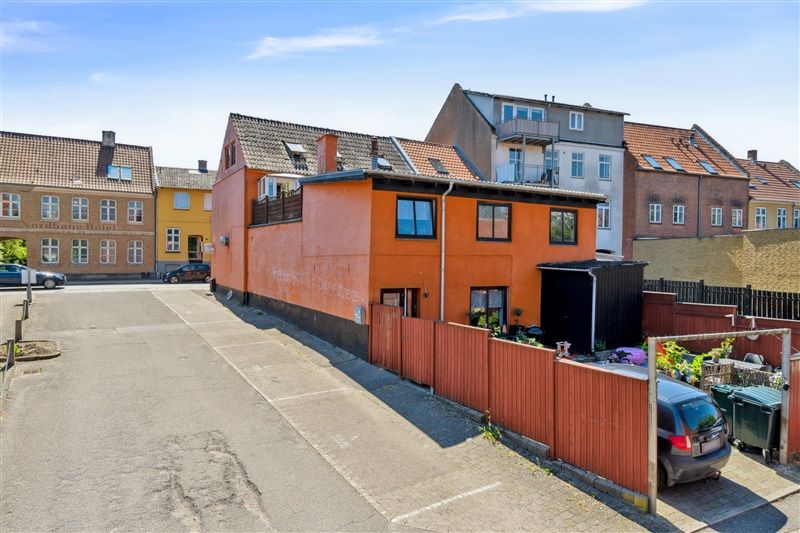 På Låsbygade 82A i Kolding er der en ejendom med røde facader og en parkeringsplads med en brun bræmme og to biler. Der er