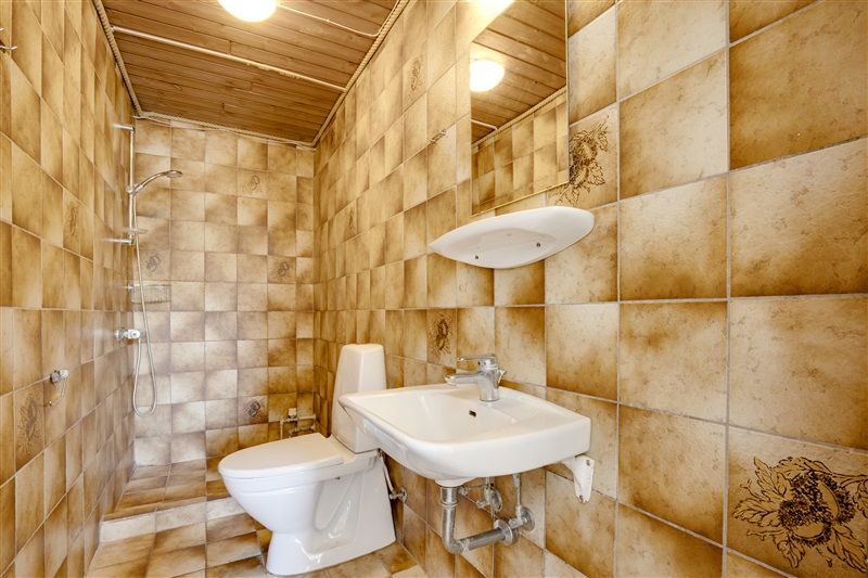 Lukket badeværelse med håndklædetørrer, gulvtøj, toilet, håndvask og bruser samt lysegult belagt væg- og loftsbeklædning