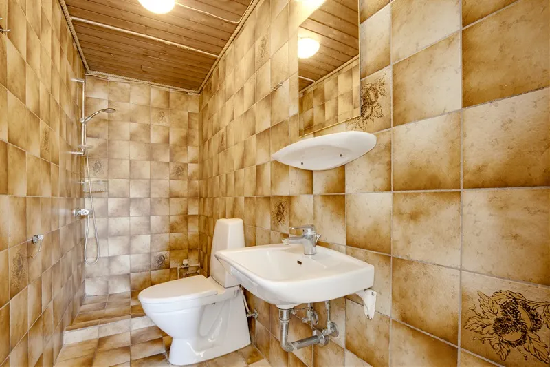 Lukket badeværelse med håndklædetørrer, gulvtøj, toilet, håndvask og bruser samt lysegult belagt væg- og loftsbeklædning