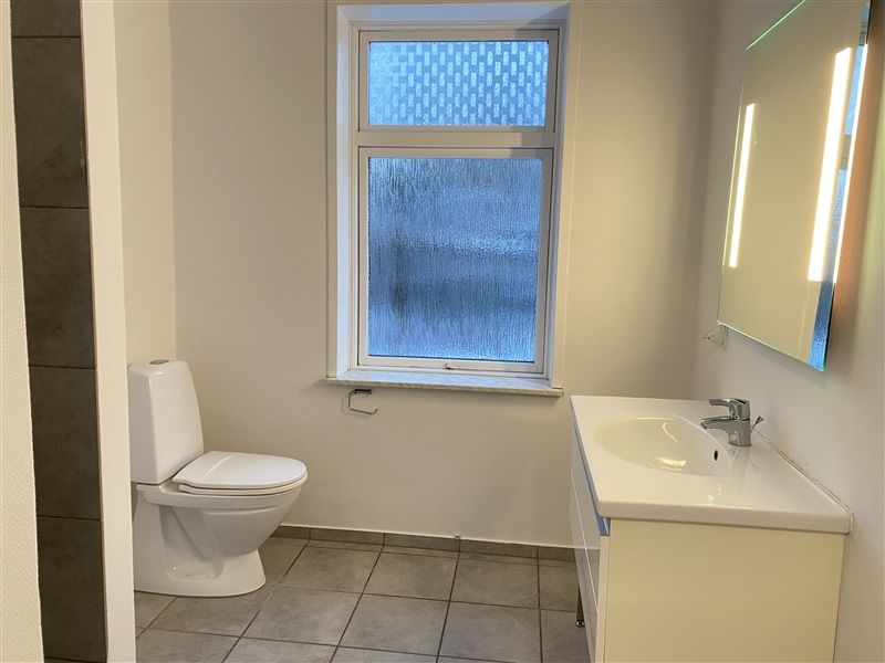 Billede af et hvidt badeværelse med toilet, håndvask, spejl og vinduesglas med rektangulært mønster